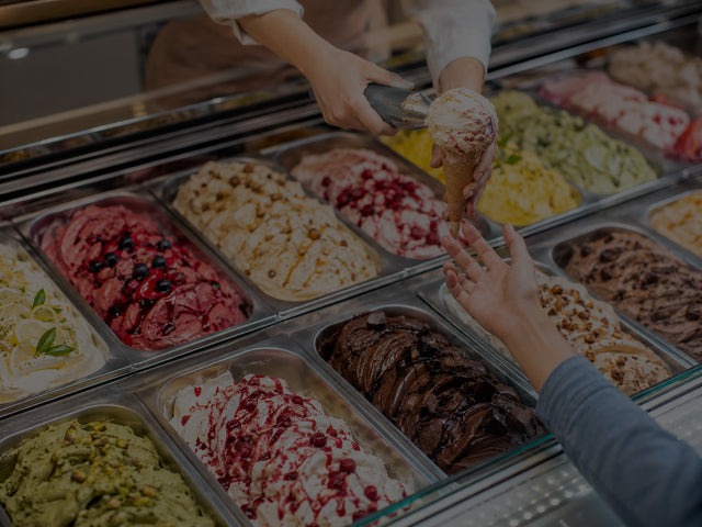A woman scooping ice cream into a cone and handing it to a customer